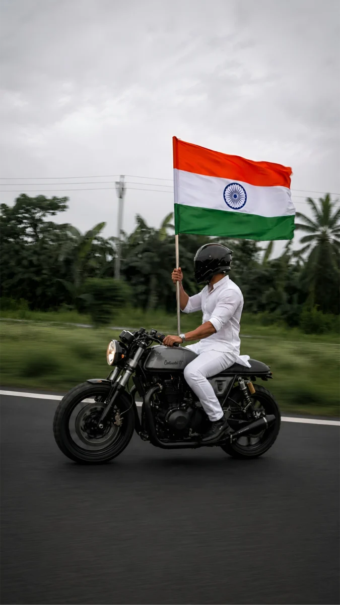 Hd image of a man riding a motorcycle holding the Indian tricolour flag on an open road, perfect for indian flag wallpaper hd, indian flag hd wallpaper, and tricolour flag wallpaper.
